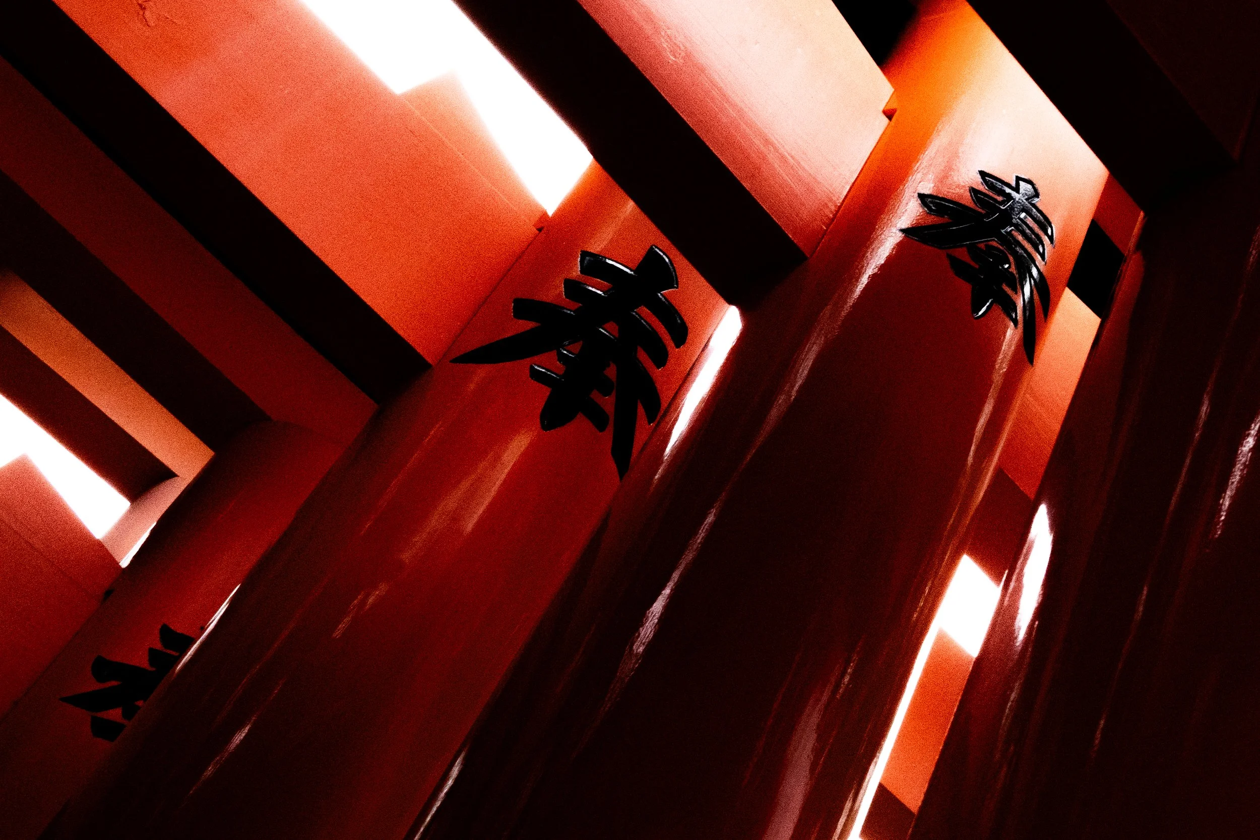 Close-up of red wooden structures with black Chinese characters and bright lights behind.