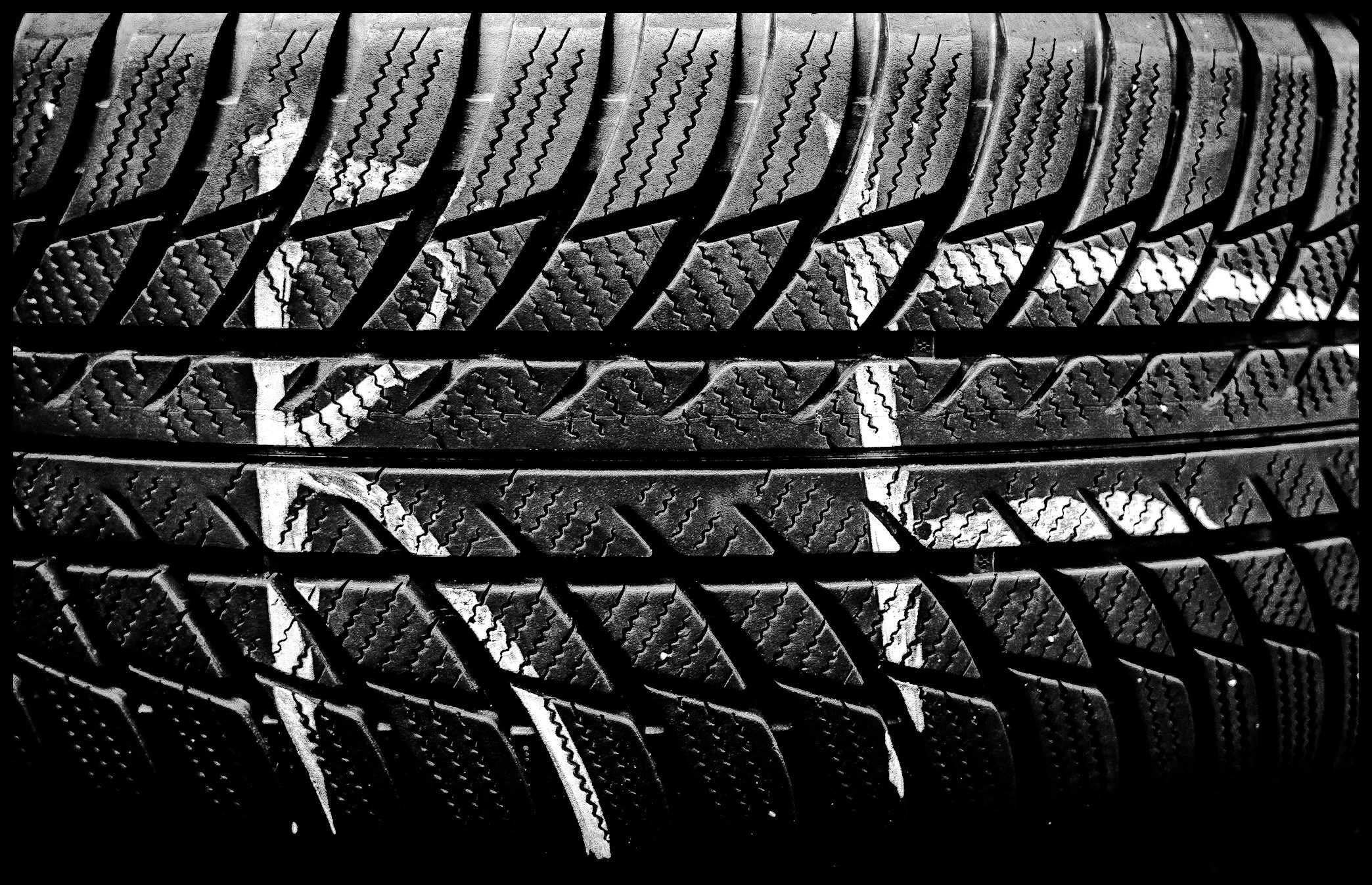 Black and white close-up of multiple car tires stacked together, showing detailed treads and patterns.