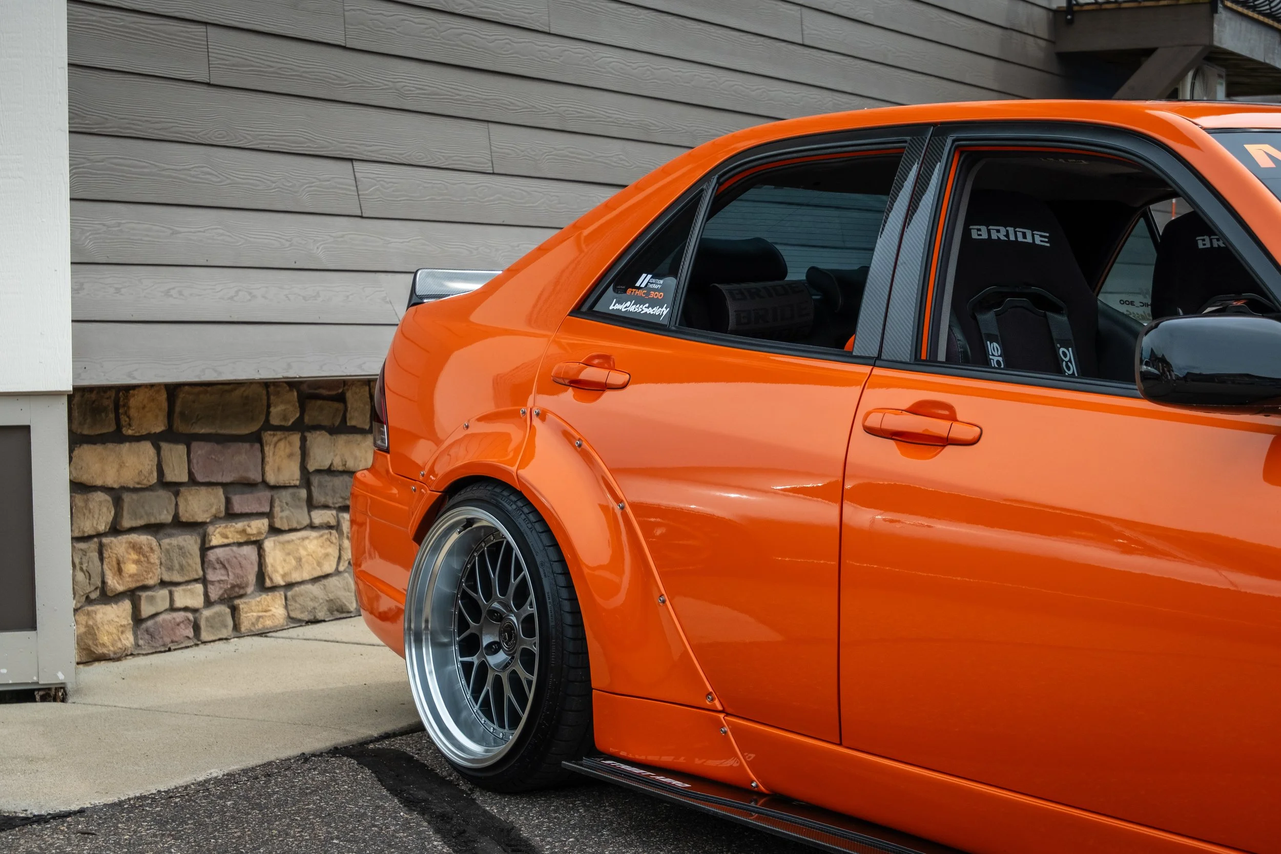 An orange sports car parked next to a building with a stone and wood exterior.