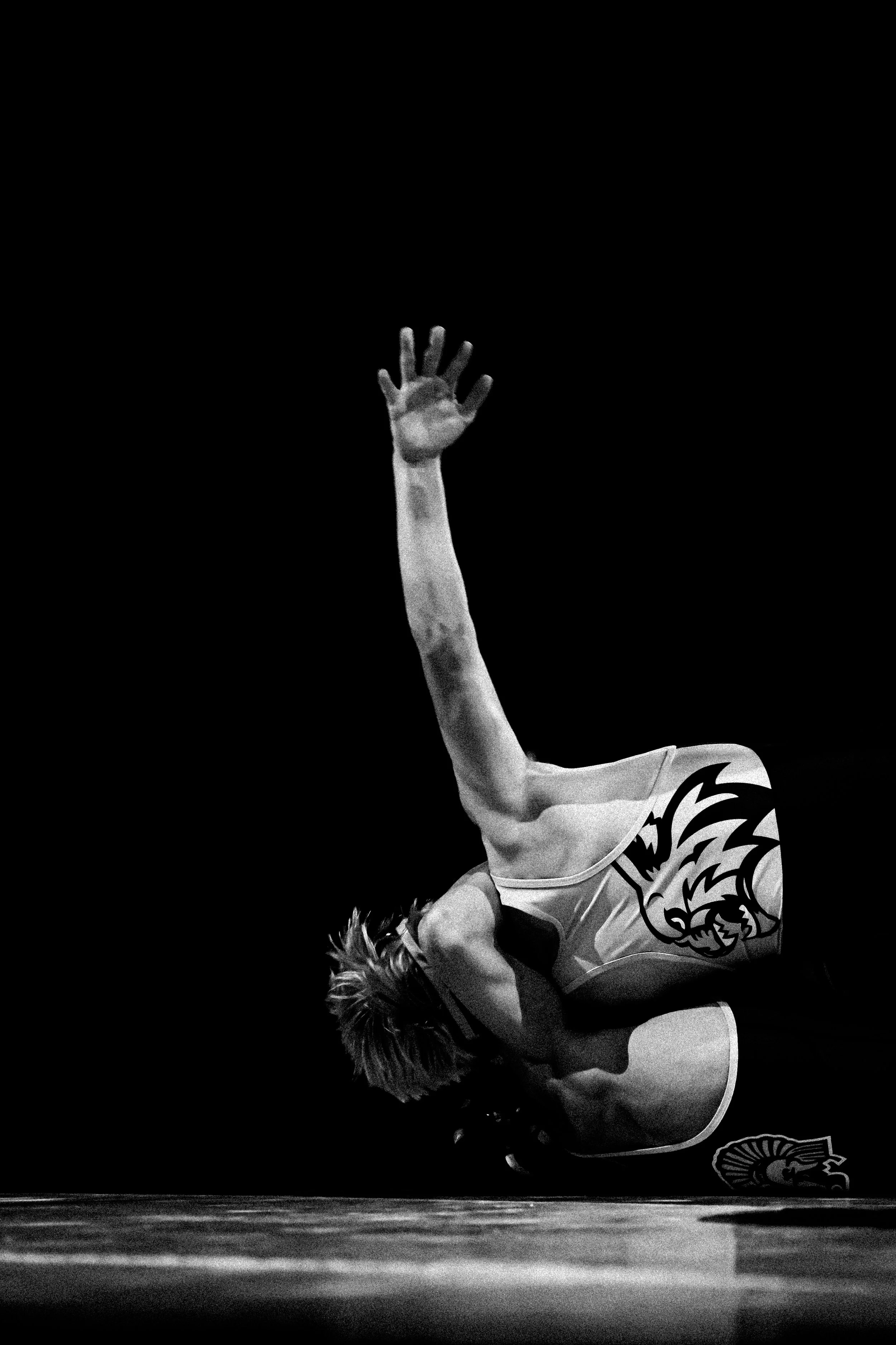 A gymnast in mid-air during a performance, wearing a leotard with a tiger graphic, against a dark background