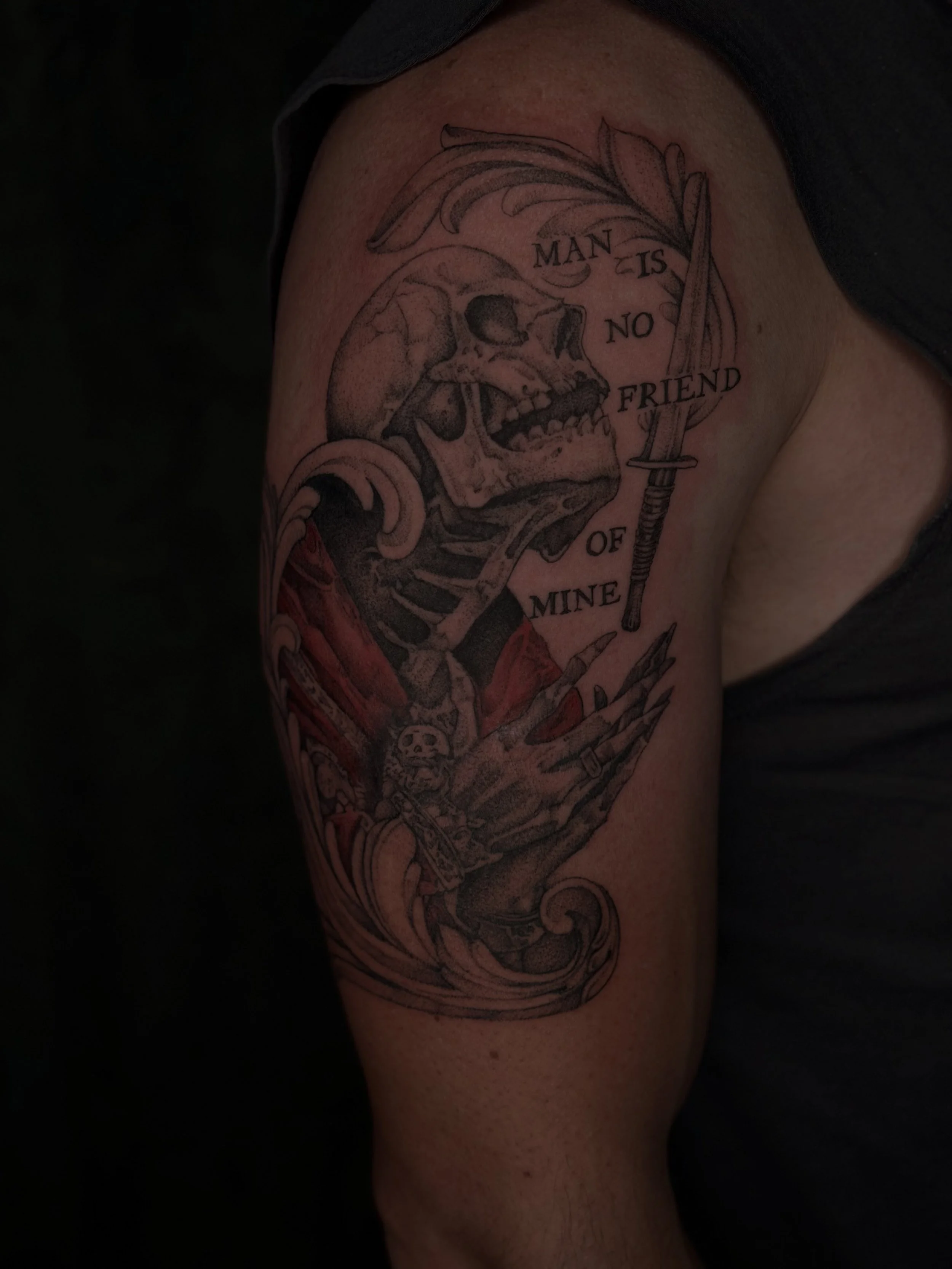 Tattoo of a human skull with a sword, with the phrase 'Man is no friend of mine' around it.