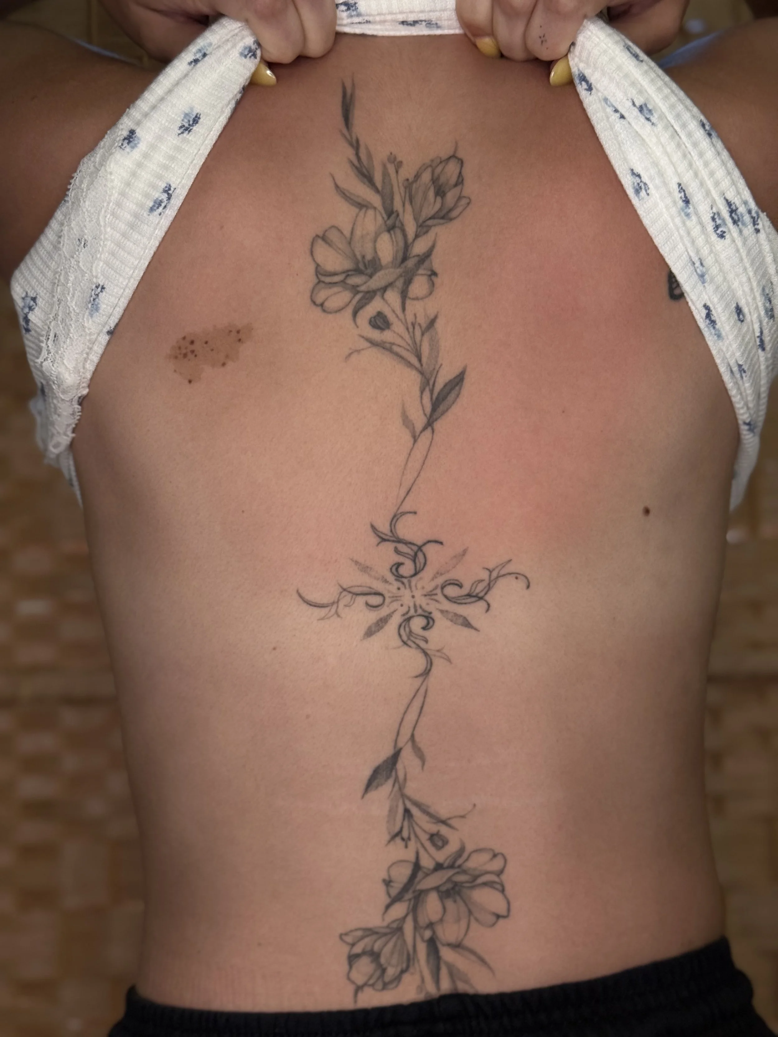 Healed fineline sun and flowers decorative ornamental black and grey spine tattoo
