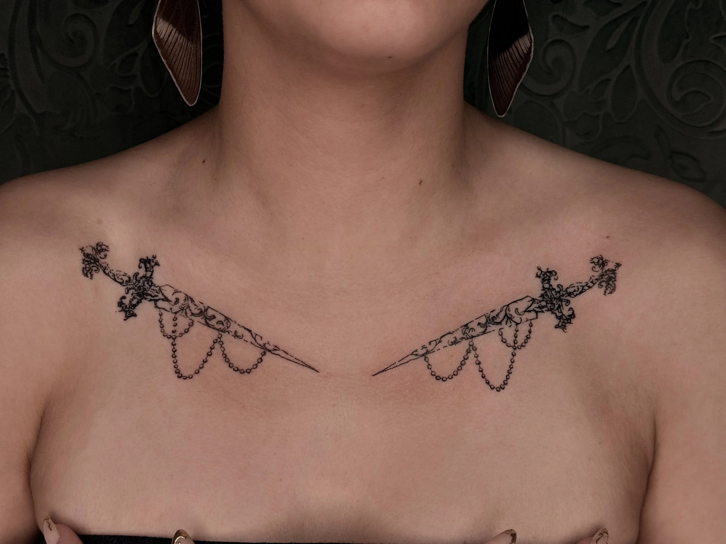 Matching collarbone daggers negative space blackwork decorative tattoos.