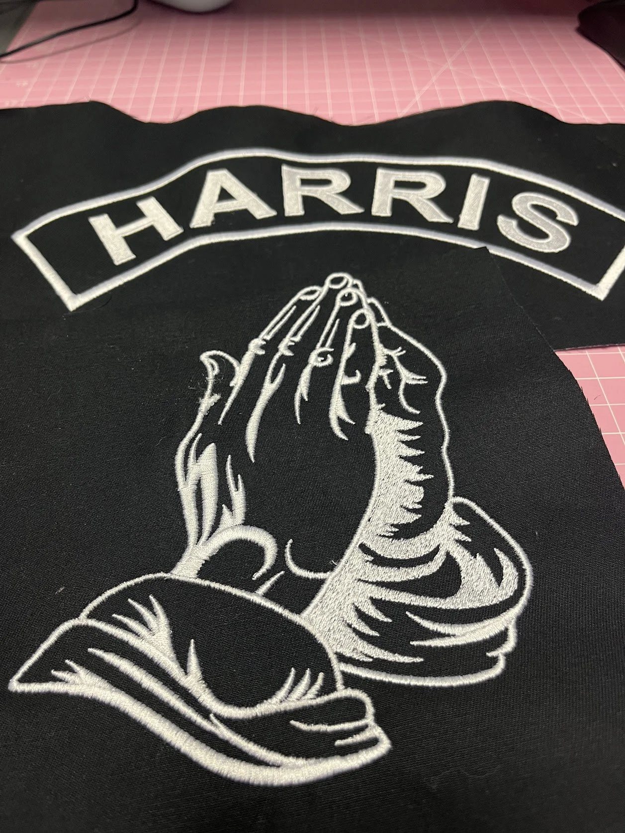 Black leather vest with white embroidered design of hands in a prayer position and the word "HARRIS" above it.