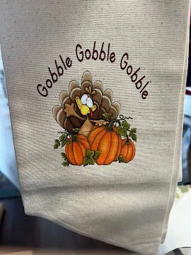 A beige wreath sash with a graphic of a cartoon turkey surrounded by pumpkins and fall leaves, with the words "Gobble Gobble".