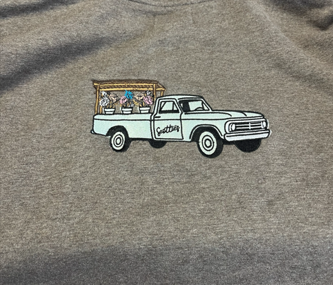 A gray sweatshirt featuring an embroidered mint green pickup truck selling varies colored flowers.