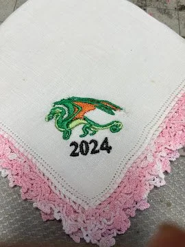 Embroidered white hankie with a green and orange dragon design, with the year 2024.