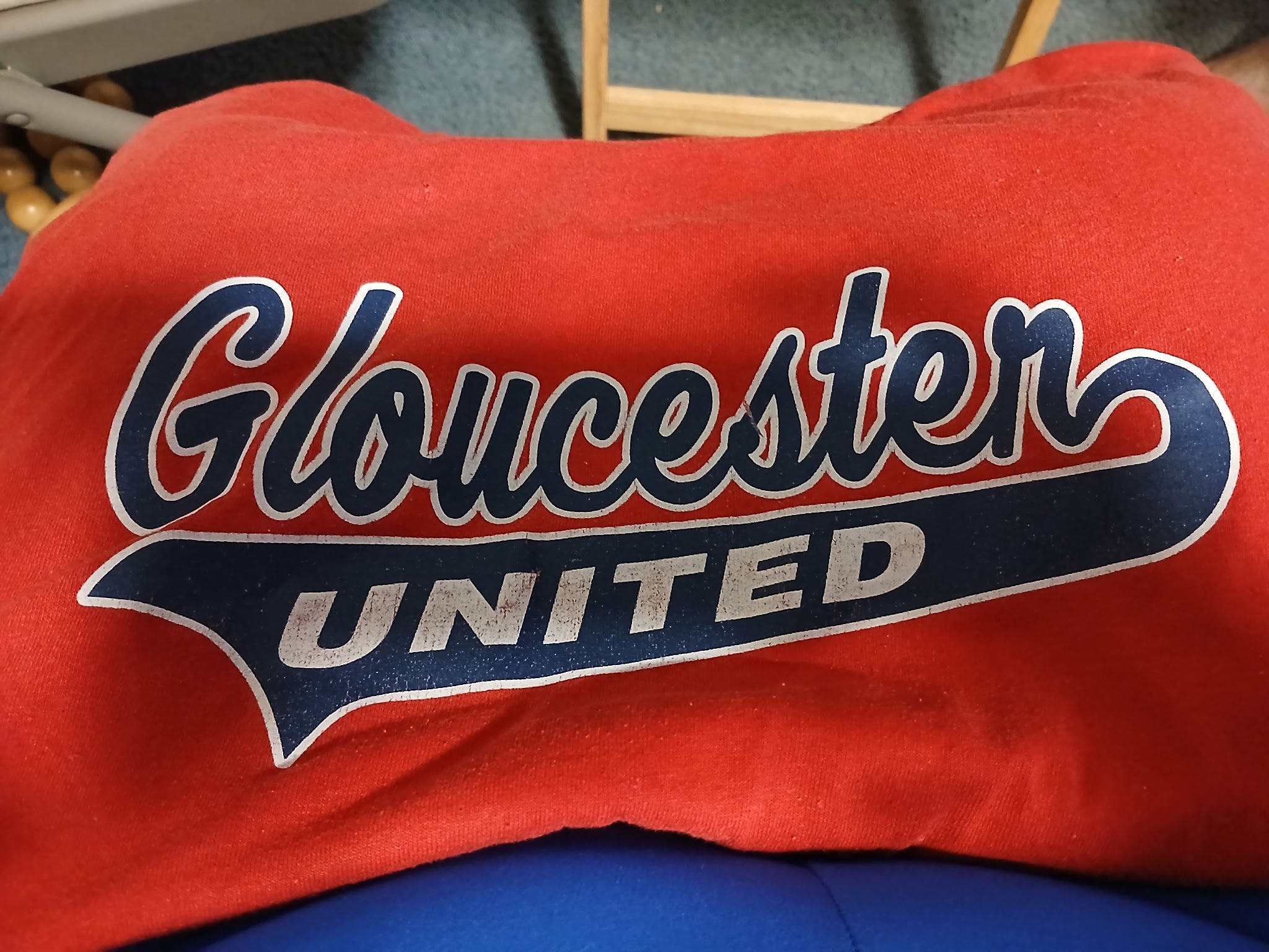 Red sweatshirt with a blue and white logo   of the Gloucester United baseball team