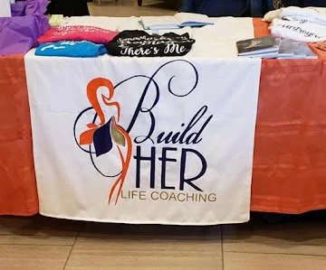 Table with a white banner displaying the logo and name 'Build HER Life Coaching' with a flamingo illustration.