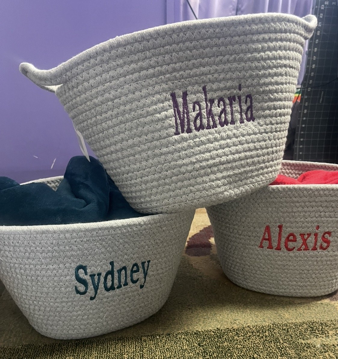 Three gray woven storage baskets with embroidered names