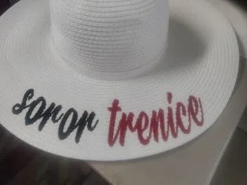 A white sunhat with the words "Soror Trenice" embroidered on the brim, in black and red thread.