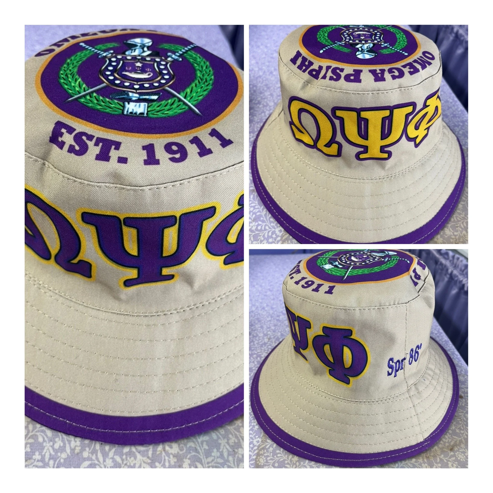 A beige bucket cap with a purple and green Omega DTF shield graphics. The front of the cap features the Omega psi logo and the side of the cap has the gold Greek letter Omega psi and with a purple border around the brim.