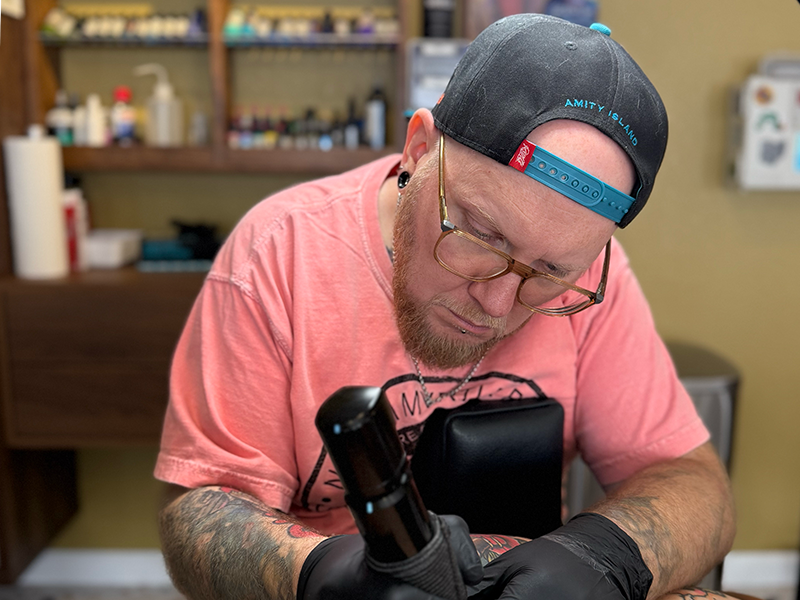 Scotty giving his client a tattoo in his booth at Eterna Tattoo.