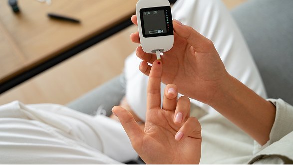 A person holding a blood glucose meter and testing their finger for blood sugar levels.