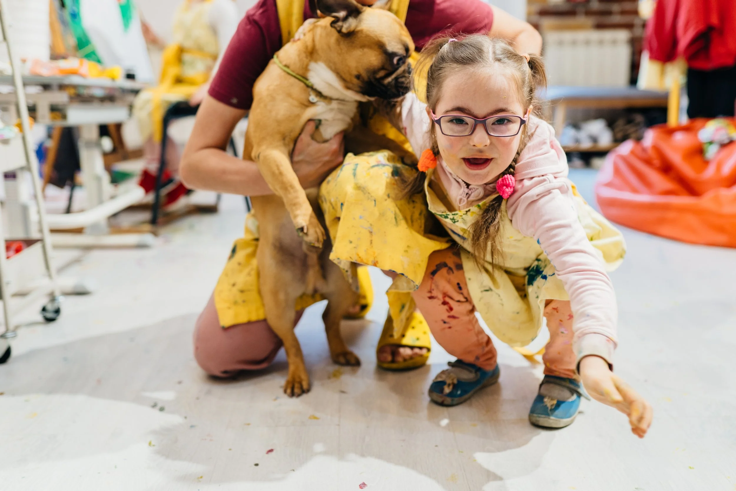 Young girls with glasses with a dog playing on the floor with paints