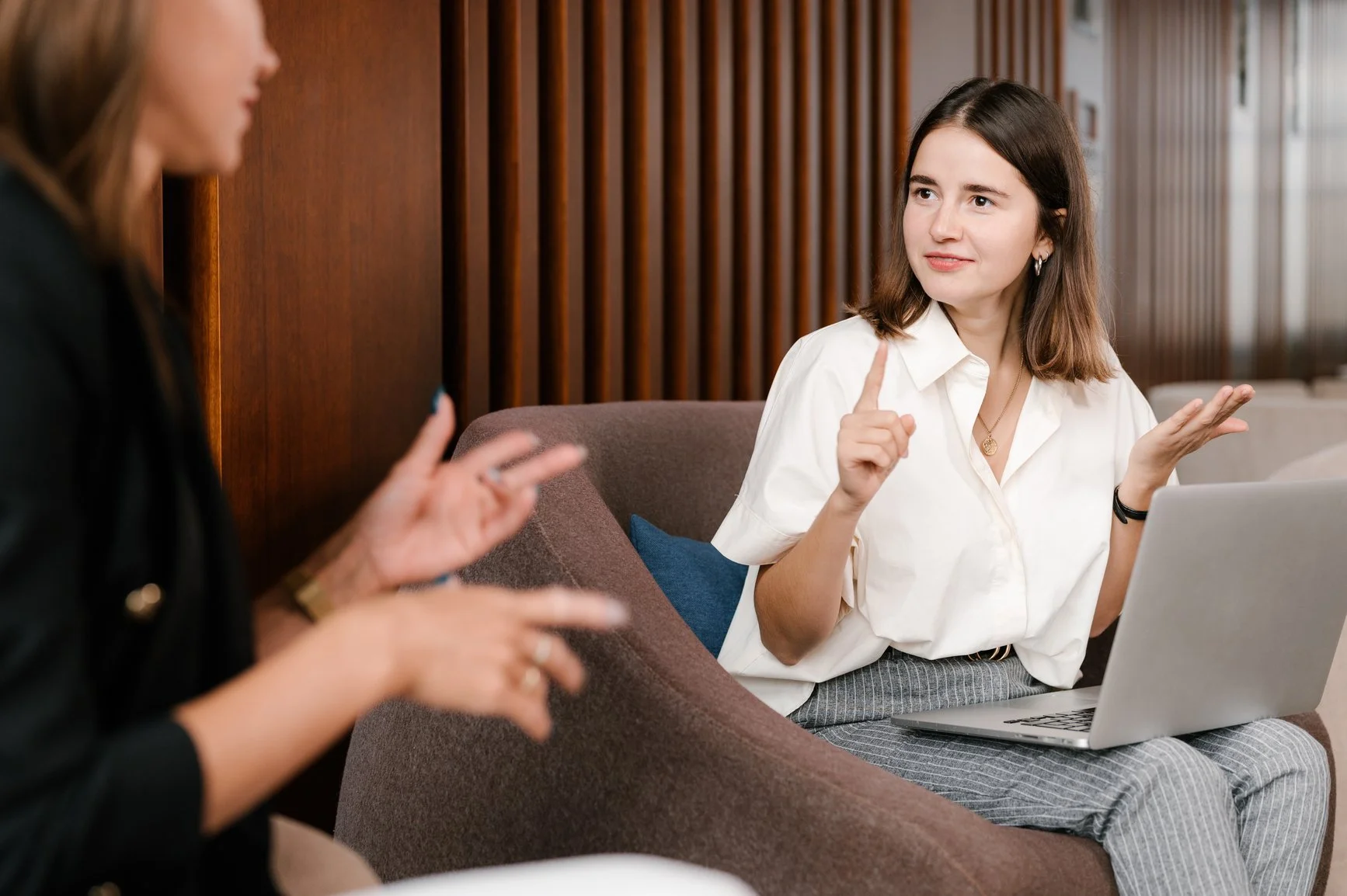 Two women sitting on lounge chairs. They are conversing using sign language.