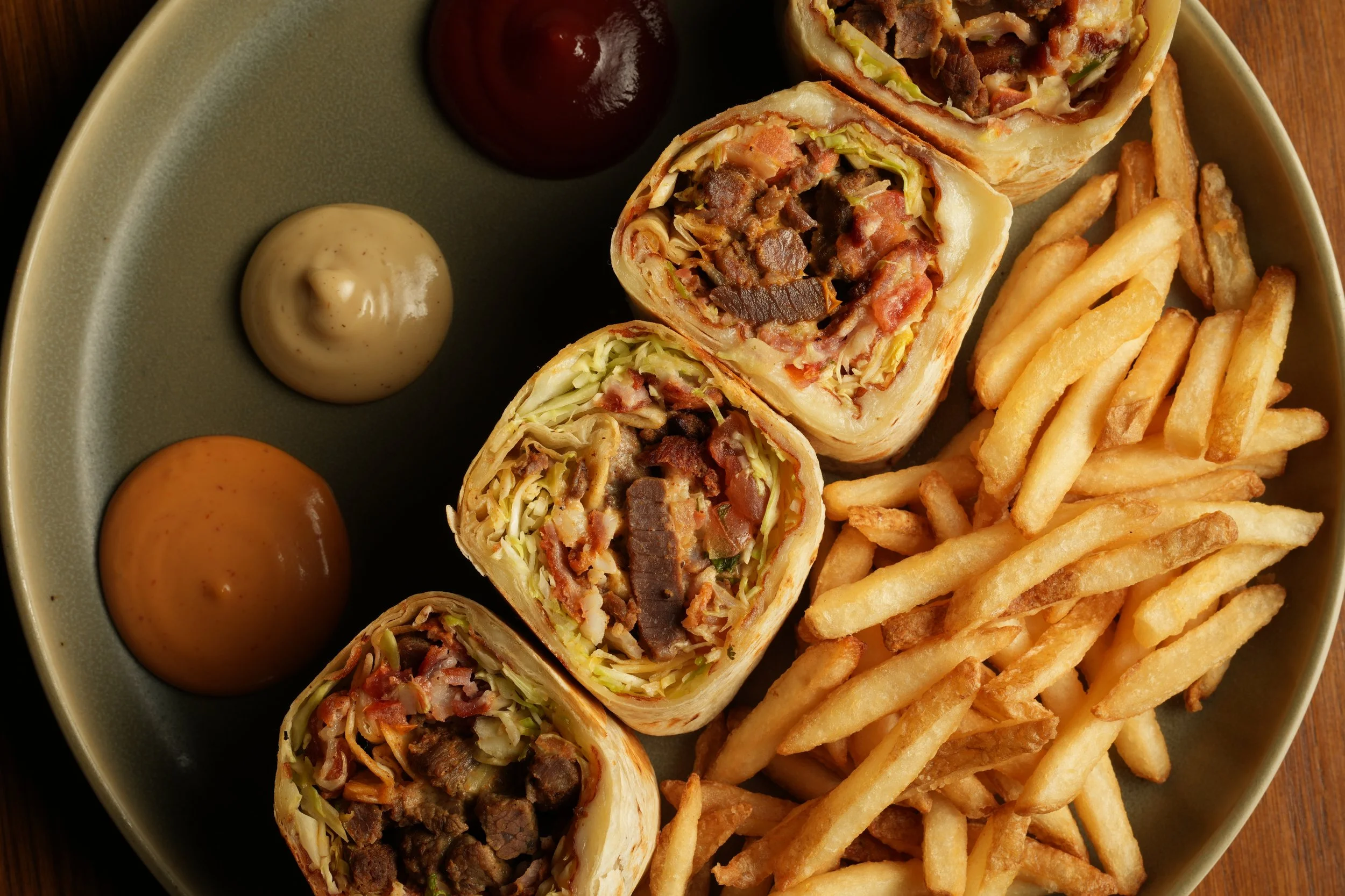 Plate with sliced burritos filled with meat, lettuce, and cheese, along with French fries and condiments.