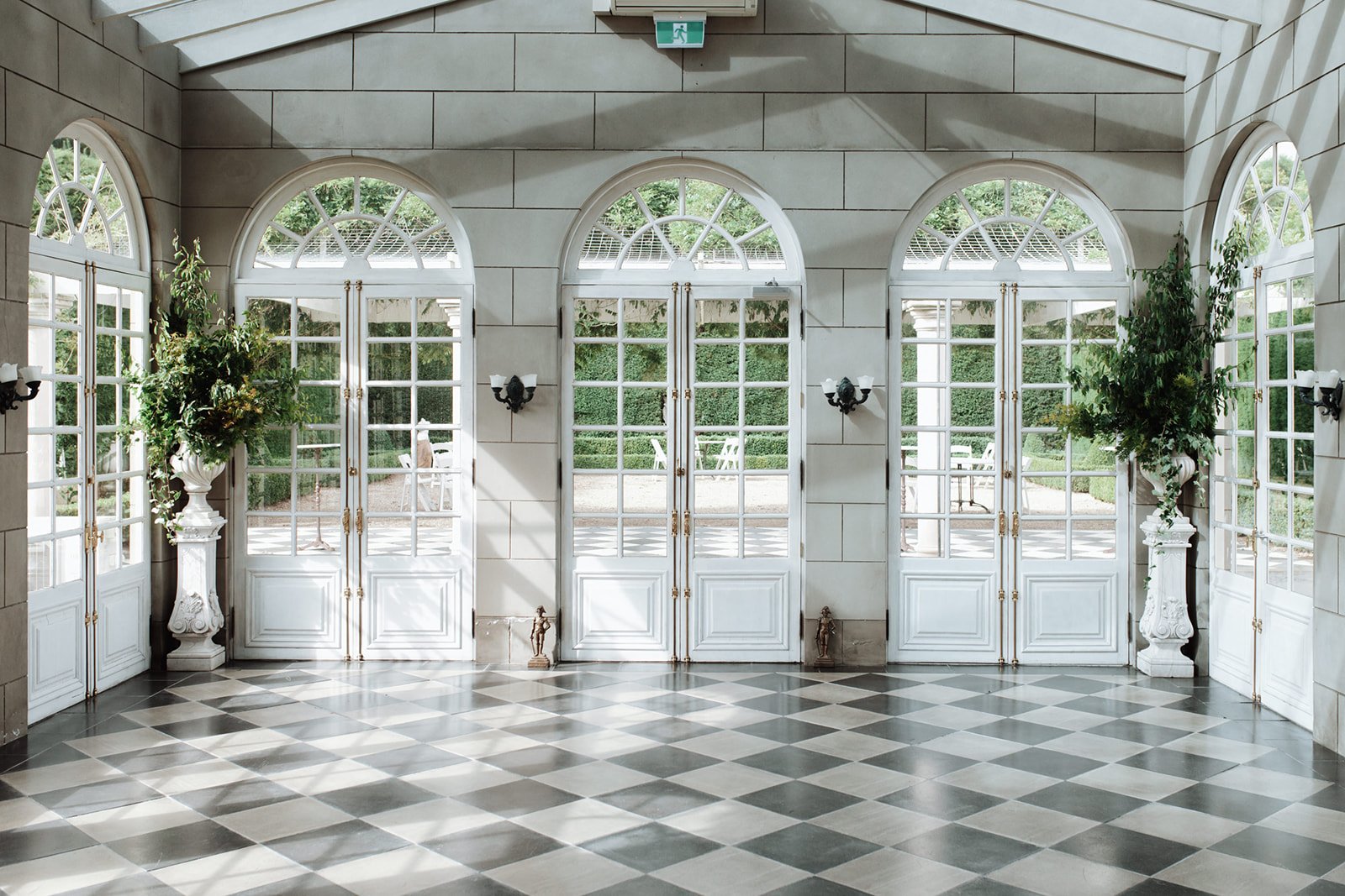 Elegant indoor space with large windows and doors, decorative plants, and black-and-white checkered flooring at a French Chateau Wedding In Campbell Point House Byron Bay.