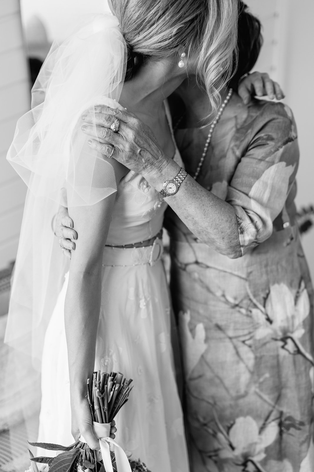 Black and white photo of a woman in a wedding dress hugging an older woman, likely her mother, in an emotional embrace. They are at a wedding at Figtree Restaurant in Byron Bay