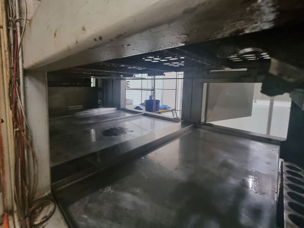 Inside a large industrial oven or kiln with metal interior, wires on the left side, and some blue objects outside the open door.
