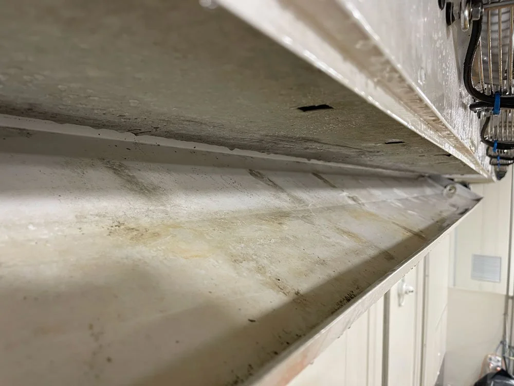 Close-up of a worn, stained metal shelf with a dirty, greasy surface in a commercial kitchen or storage area.