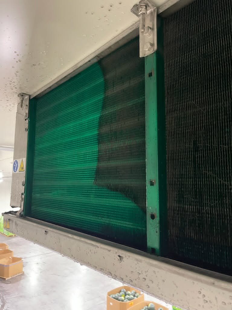 Large industrial air conditioning or refrigeration unit with green and black heat exchanger fins, mounted in a concrete room.