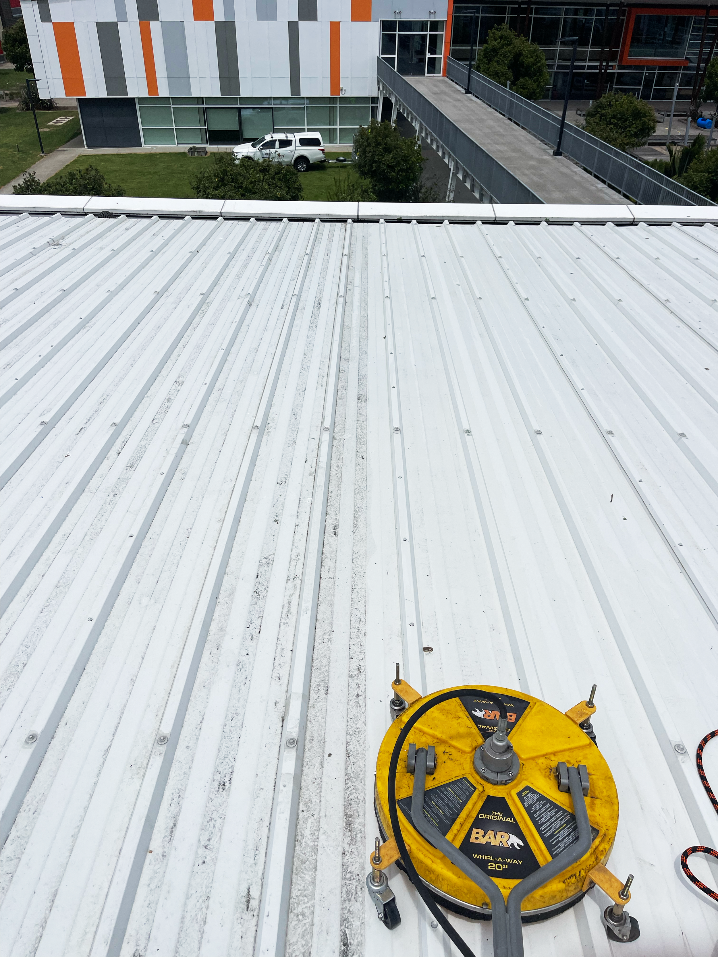 View of a white metal roof with a yellow and black construction tool on it, used for installing solar panels or roofing work.