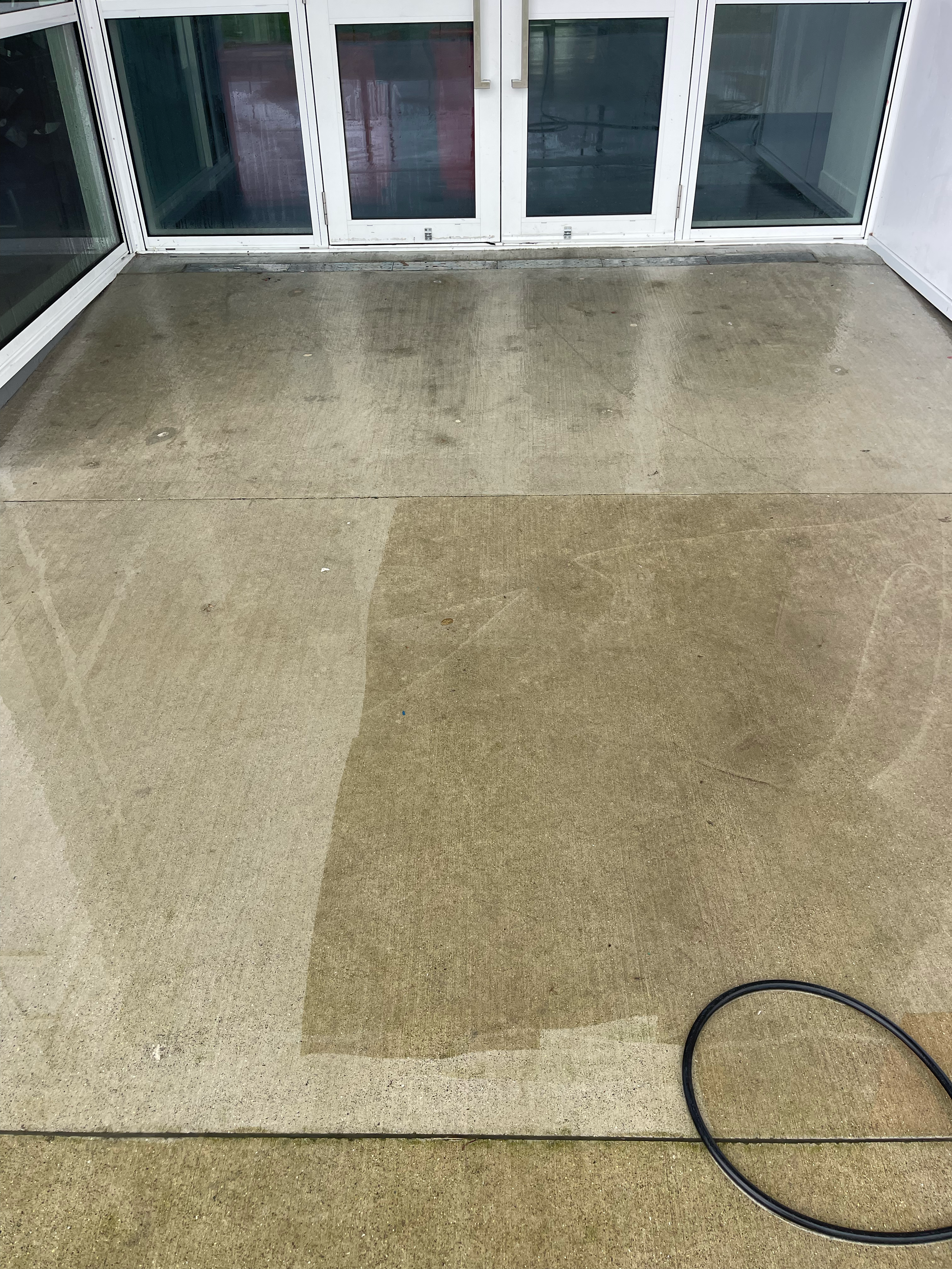 Freshly cleaned concrete patio with water streaks and a black hose on the right side.