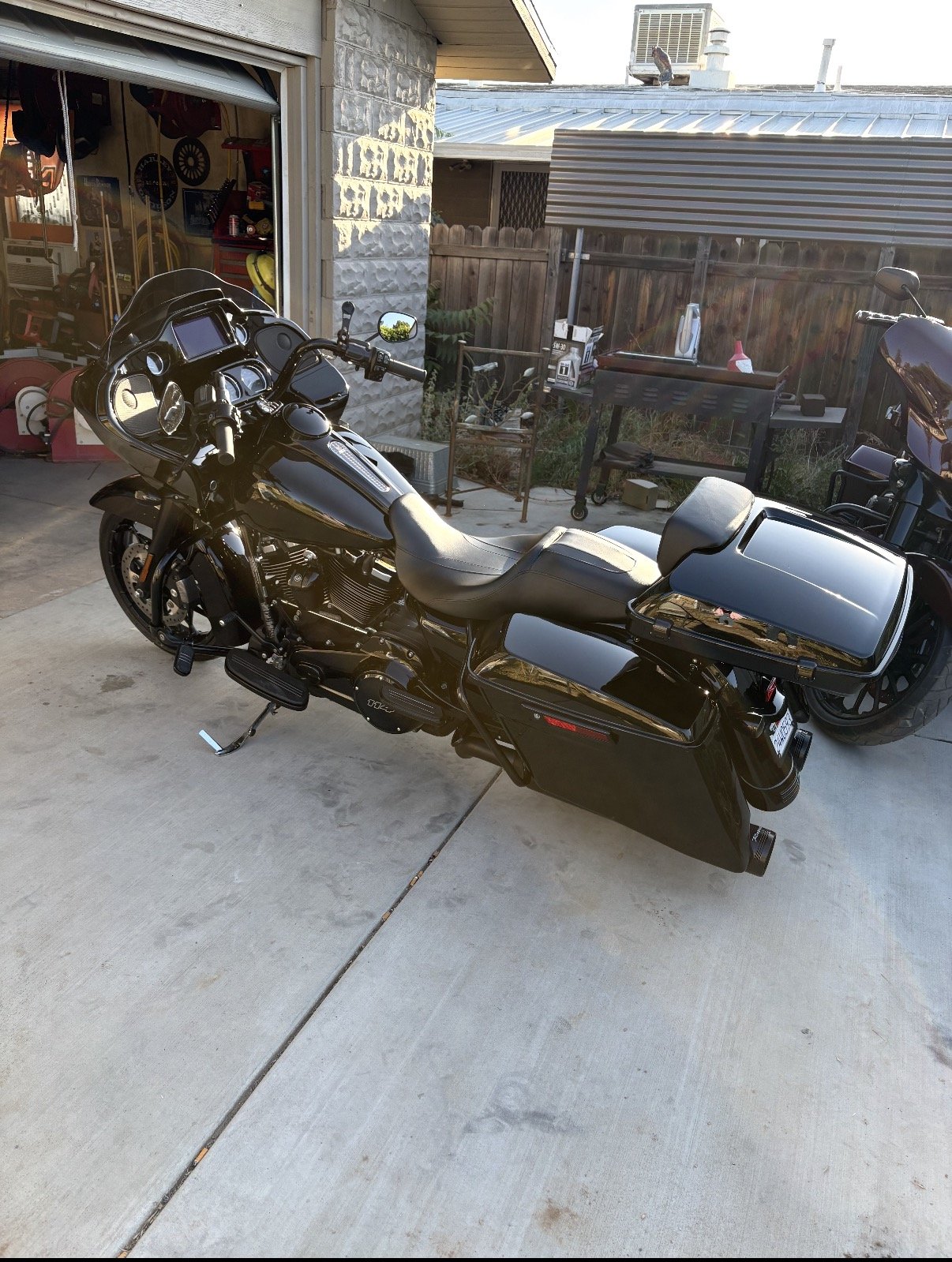 Black touring motorcycle parked on driveway outside a garage, with a stone wall and wooden fence in the background.