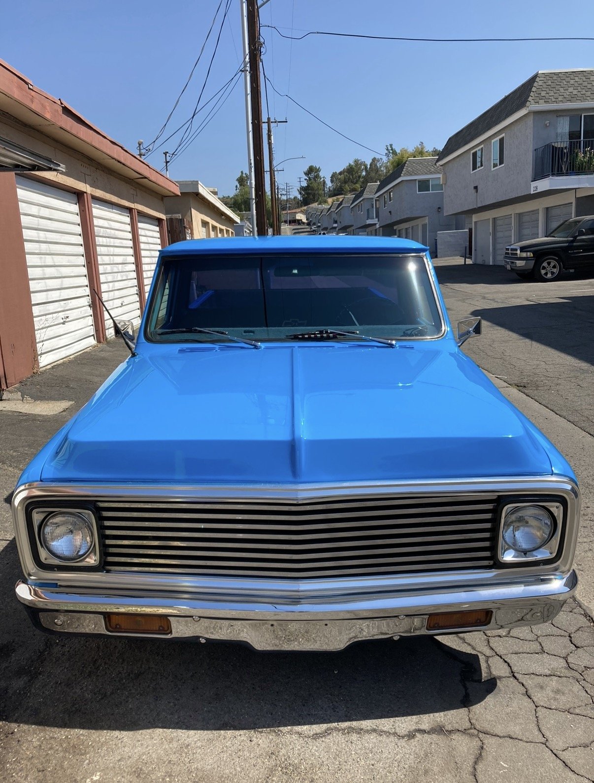 Front view of a blue vintage car parked outdoors on a sunny day with houses and power lines in the background.