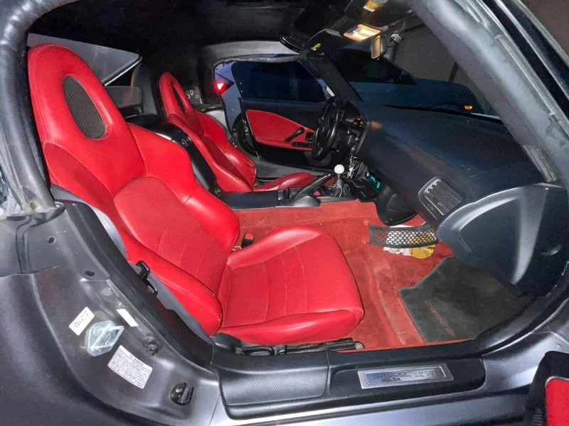 Interior of a sports car with red racing seats, black dashboard, and red carpet, showing the driver's side from the passenger's side.