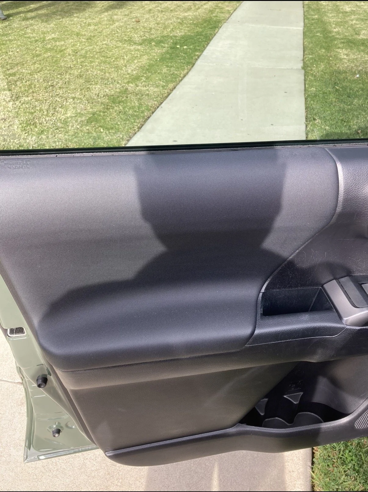 Close-up of a car door interior with black textured panel, window, handle, and a reflection shadow.