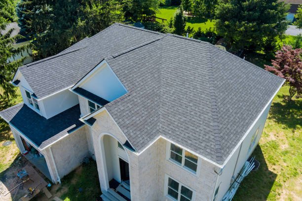aerial view of a two-story house with a gray shingle roof and white exterior walls surrounded by green trees and lawn.