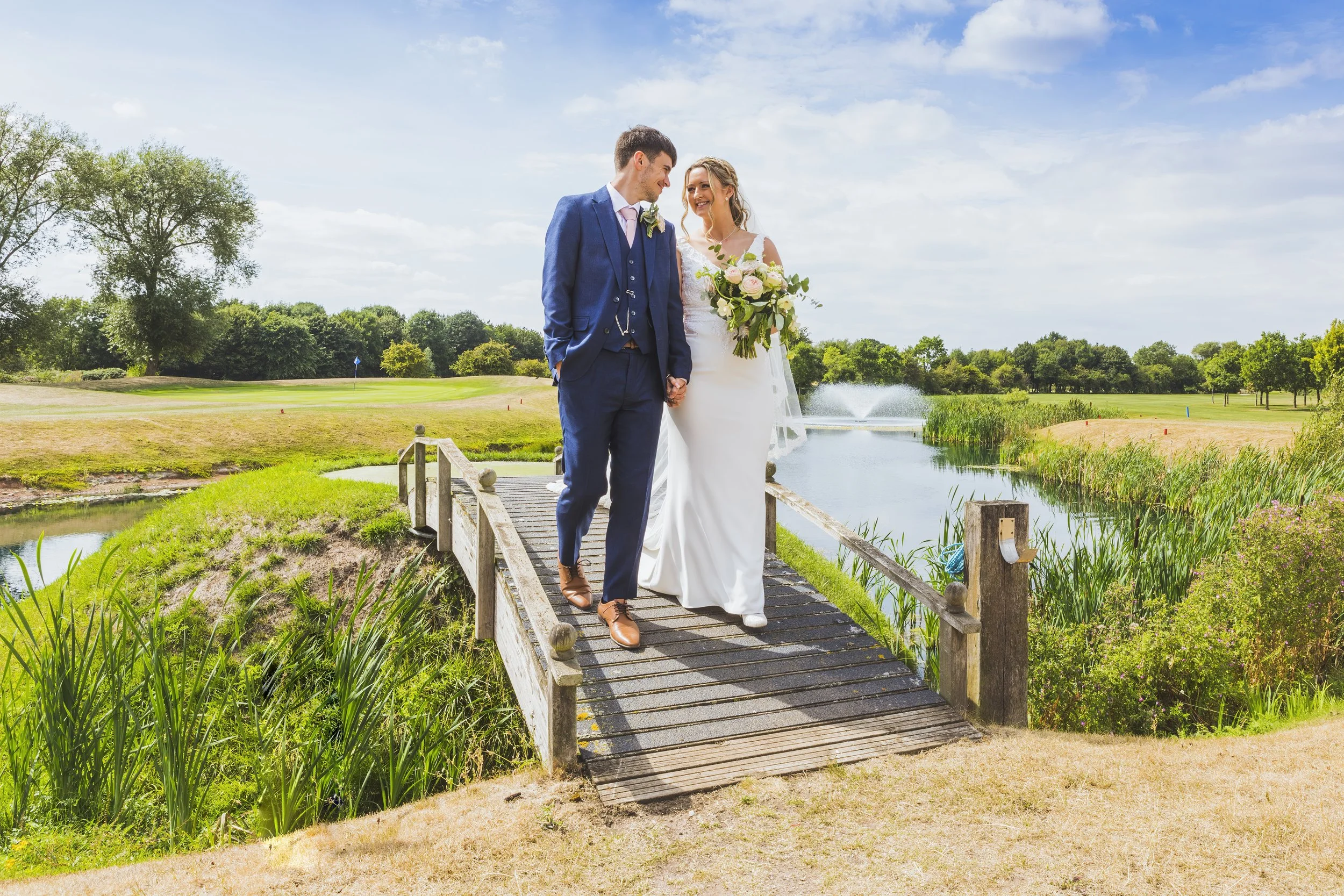 Bride and groom take a romantic stroll over a small bridge at a golf course. @GlennMatherPhotography