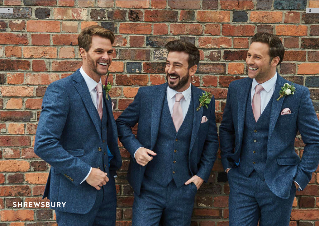 Three men in blue suits and light pink ties standing in front of a brick wall, smiling and laughing.