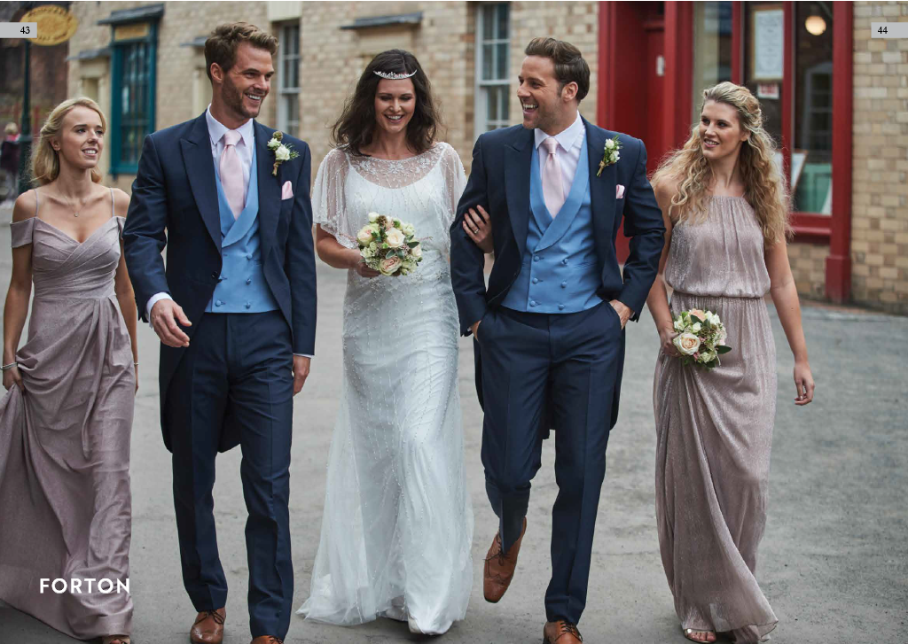 A group of six people, including a bride and groom, walking and smiling outdoors on a city street, dressed in wedding attire.