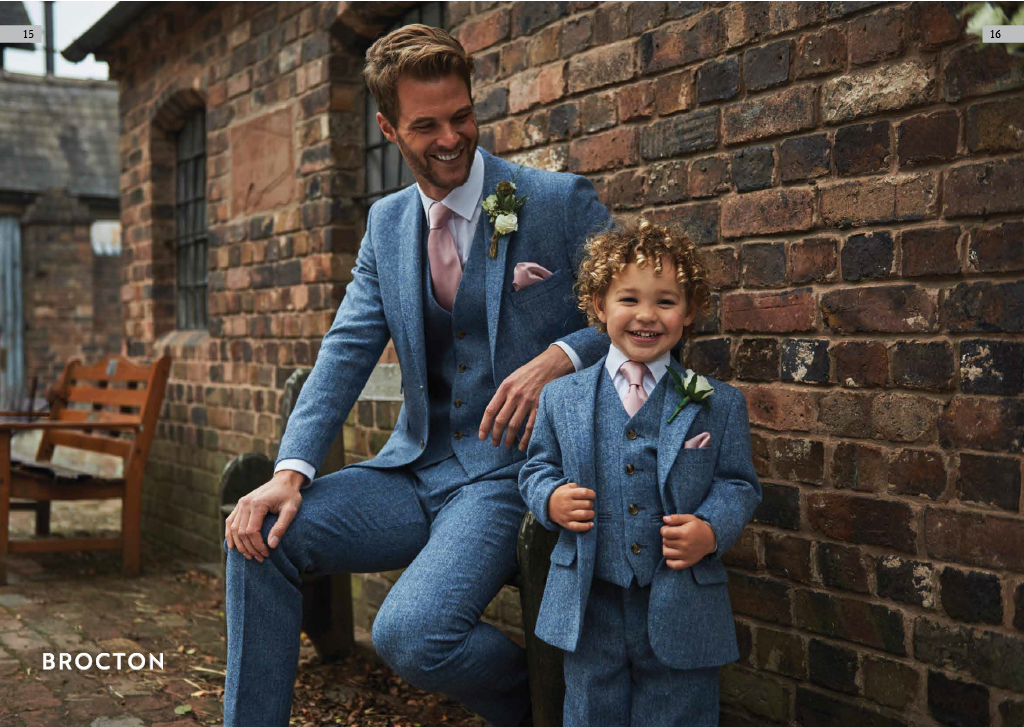 A man and a young boy in blue suits with pink ties smiling and laughing outdoors against a brick wall.