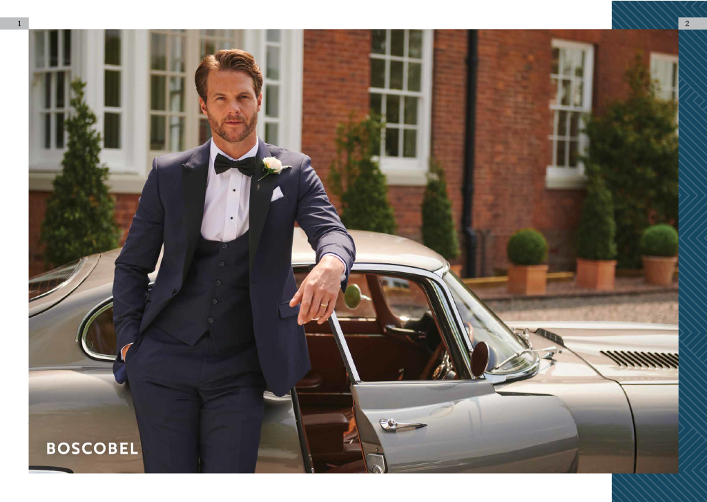 Man in tuxedo leaning against vintage car in front of brick building with potted plants.