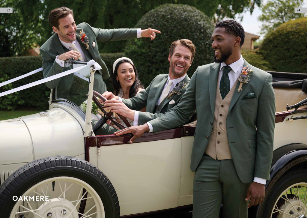 A group of four friends dressed in vintage suits, enjoying a ride in a classic open-top car outdoors during daytime.