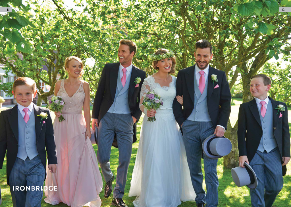 A wedding party walking outdoors among green trees, with the bride and groom in the center, surrounded by bridesmaids and groomsmen all dressed elegantly and smiling.