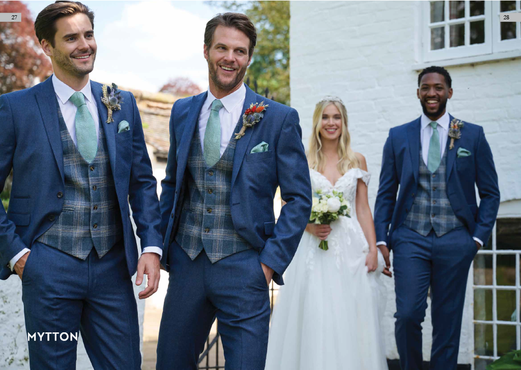 Four people dressed in wedding attire standing outside, with men in blue suits and a woman in a white wedding dress holding a bouquet of flowers, smiling.