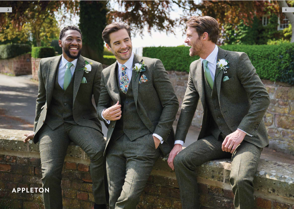 Three men in gray suits with ties and boutonnières sitting on a brick ledge outdoors, smiling and talking.