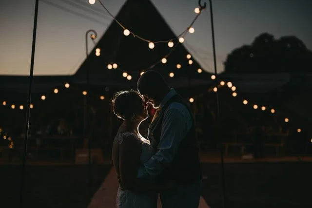 Bride and Groom in an embrace in the moonlight. The tipi is silhouetted in the background, adorned with festoon lights.