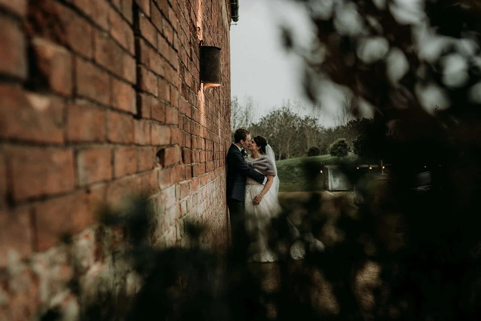 The couple are pictured outside locked in a kiss, surrounded by trees and greenery. They are leaning on an exterior wall and Deanna is wearing a shrug to keep warm.
