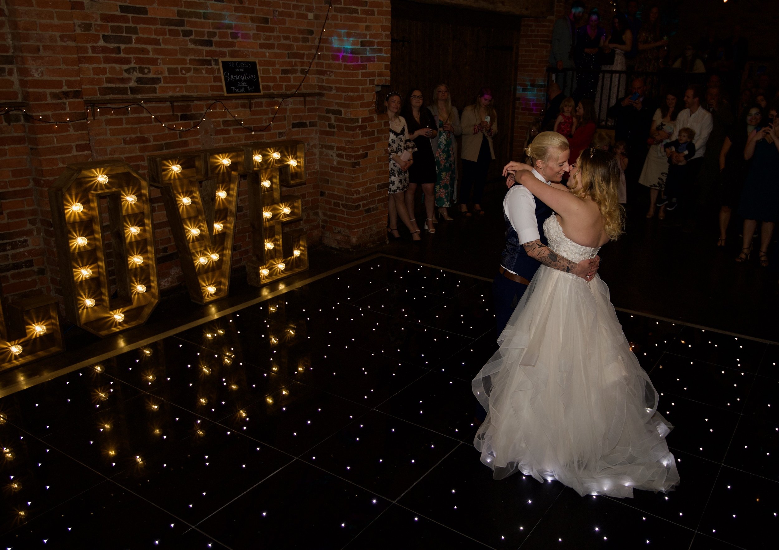 The couple dance next to large letters spelling out LOVE. They are gazing at each other full of love.