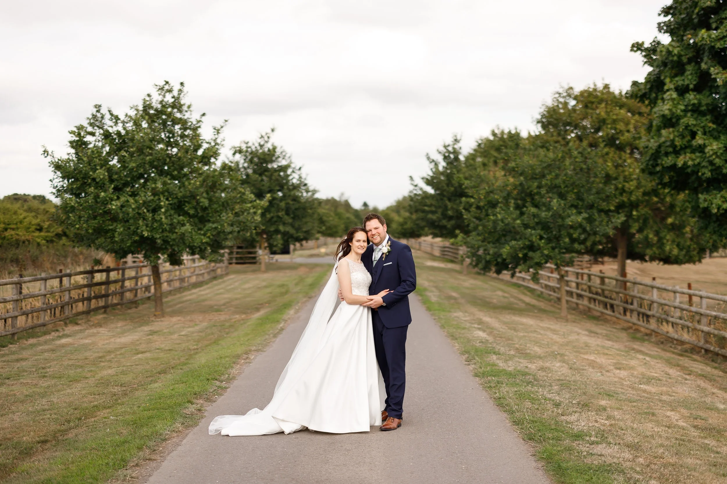 The bride and groom embrace outside on the driveway to the venue. Rachel is wearing a long A-line gown with a beaded bodice - Catherine by Ellis Bridal - and a long sweeping veil.
