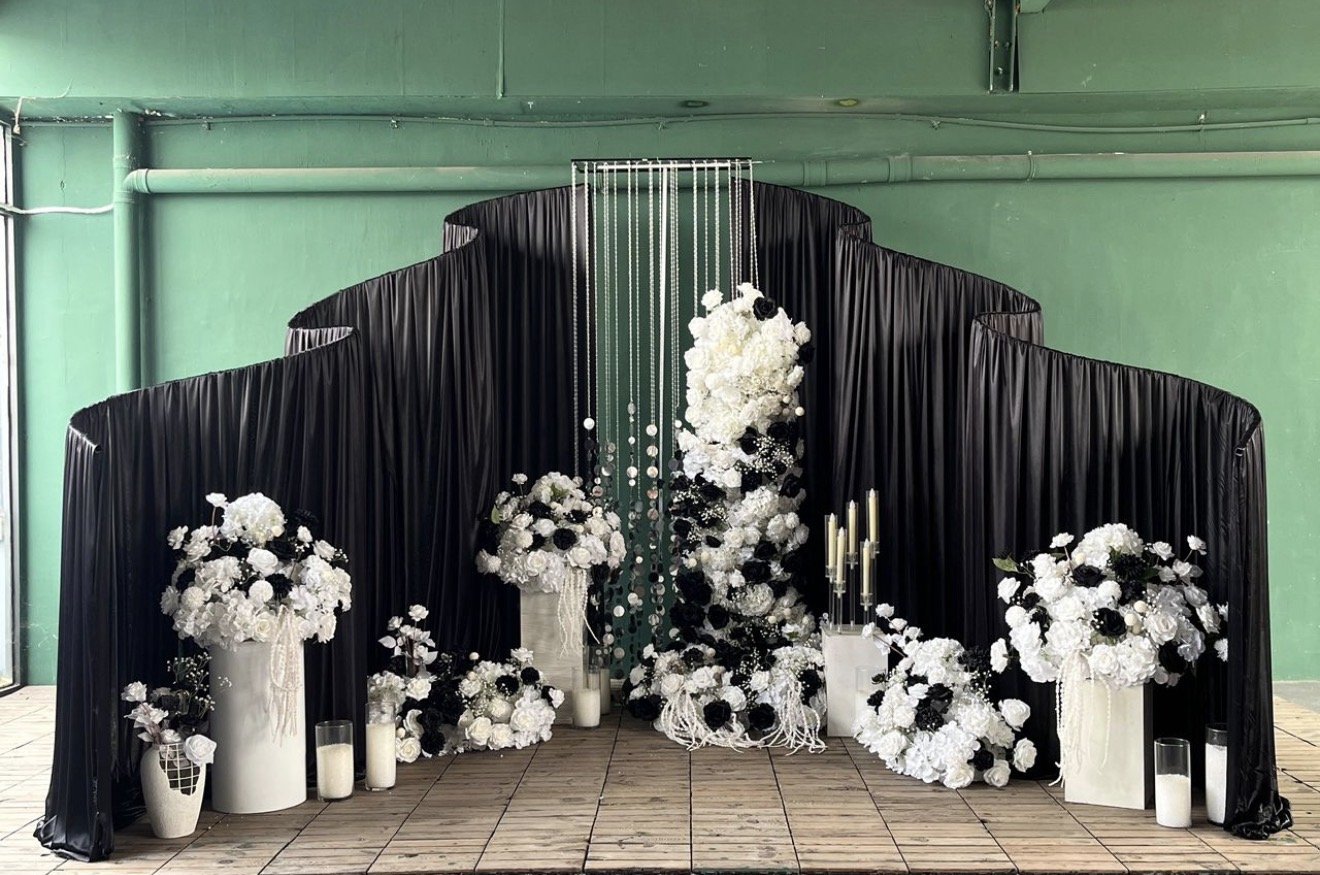 Elegant floral arrangement with white and black flowers, candles, and black drapery backdrop.