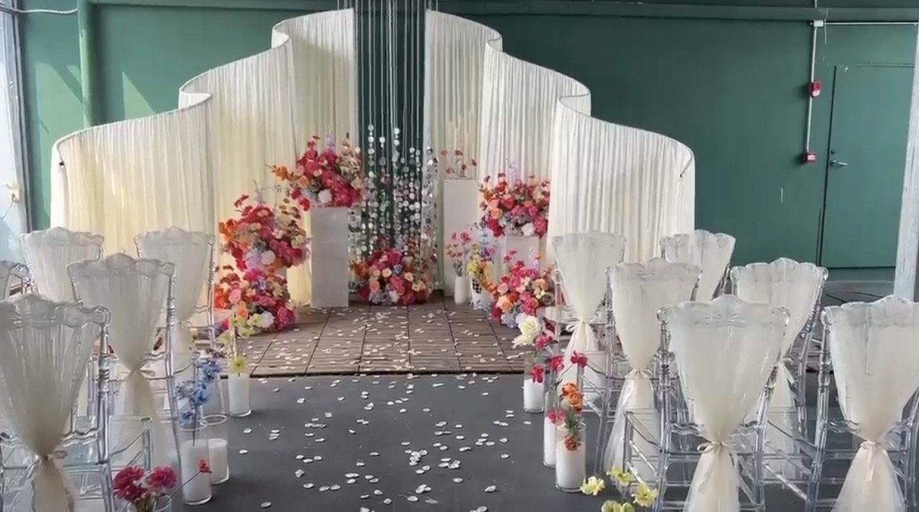 Wedding ceremony setup with white chairs, floral arrangements, and a curtain backdrop.