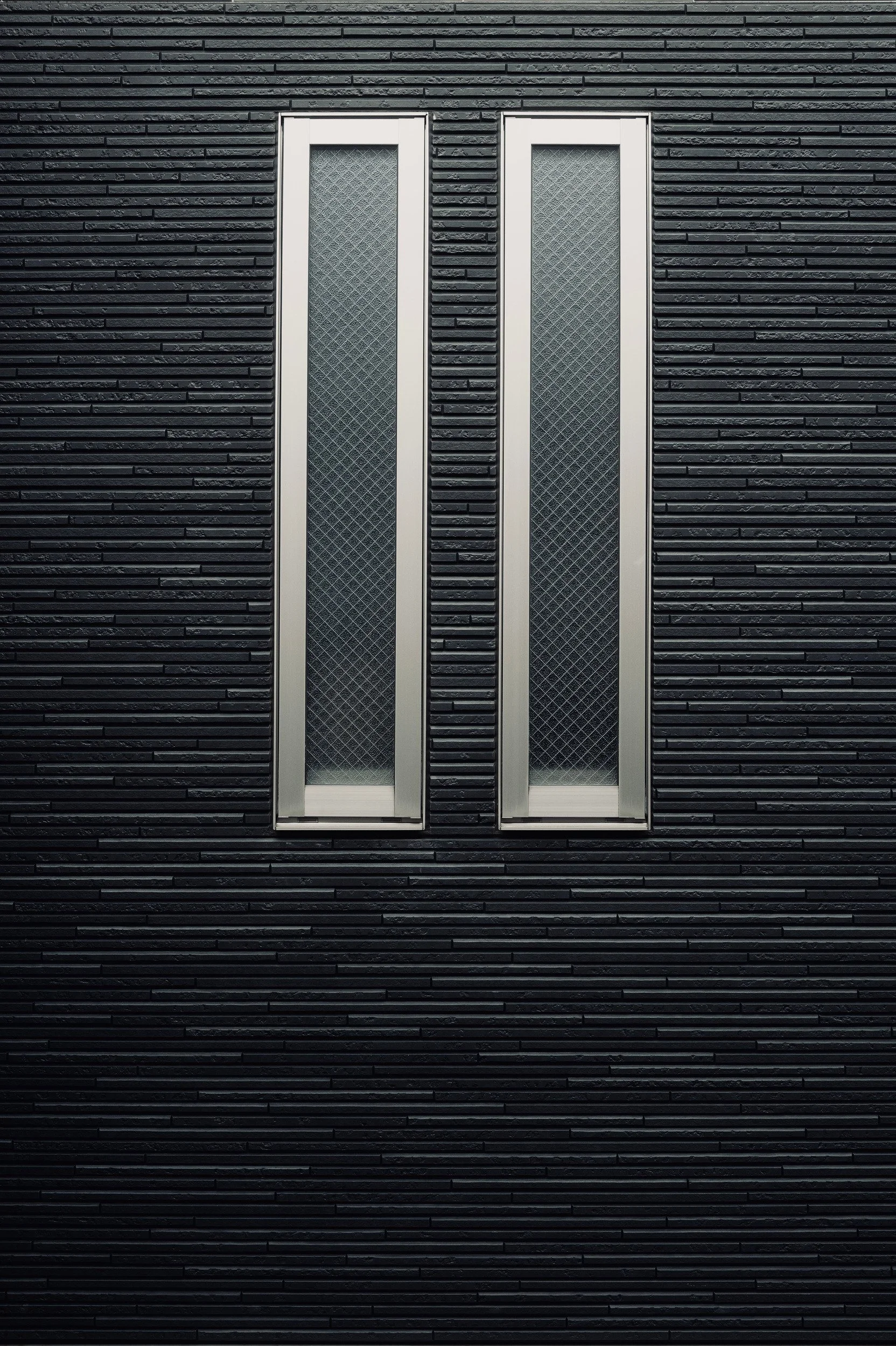 Two narrow wired-glass windows set in a dark horizontally ribbed wall.