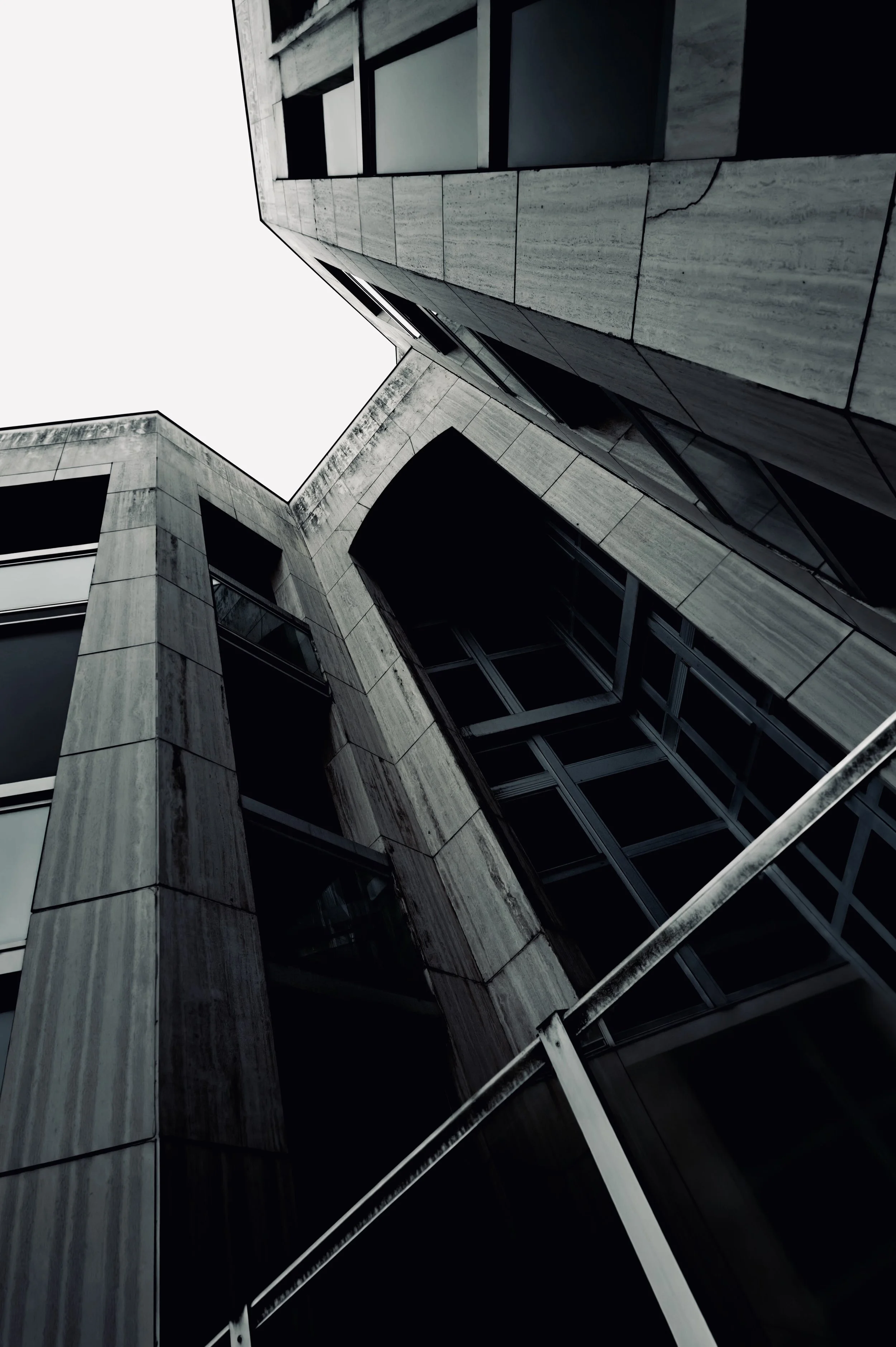Upward view of angular concrete and glazed building facades meeting against a light sky.